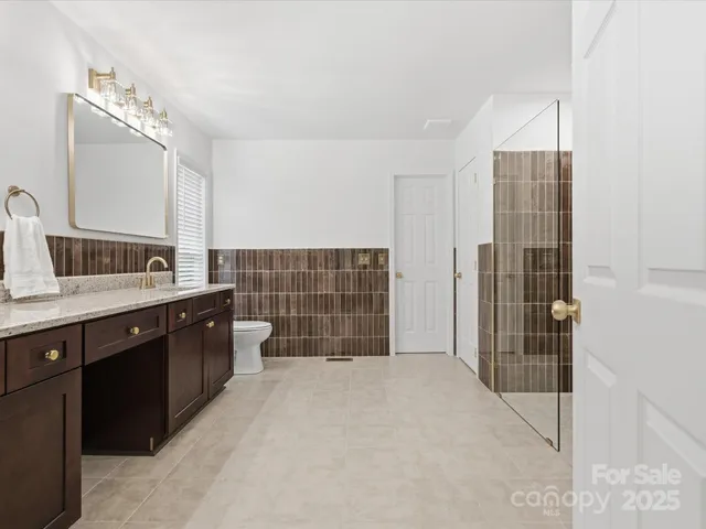 a spacious bathroom with a double vanity sink a toilet a mirror and shower
