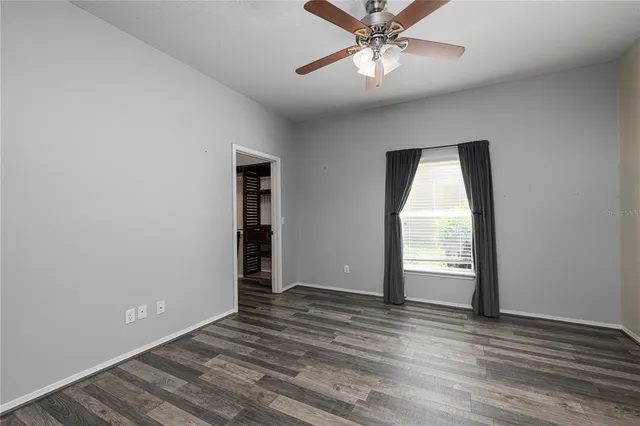 an empty room with wooden floor fan and windows