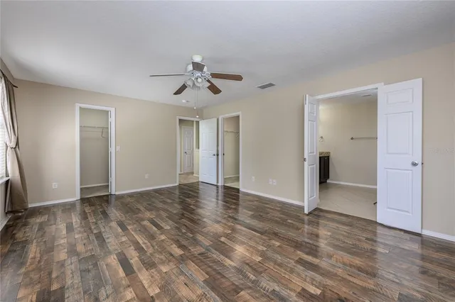 a view of an empty room with wooden floor and a ceiling fan