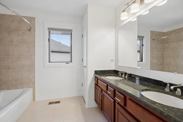 a bathroom with a granite countertop double vanity sink and a bathtub
