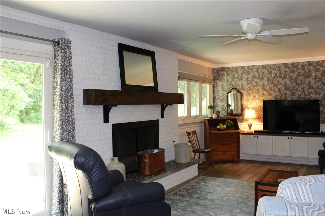 5547 River Styx Road Medina, OH 44256 - Photo 15 of 45 Living area featuring a white brick fireplace with a wood mantel, wood-finish flooring, a ceiling fan, a patterned accent wall, and built-in cabinetry with a countertop