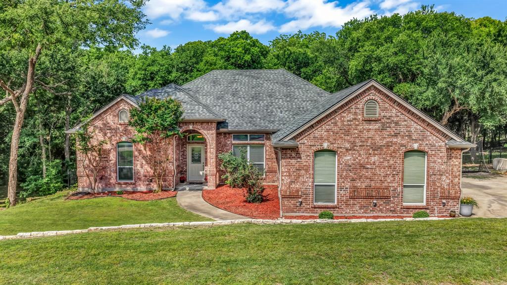 203 Mockingbird Lane Aledo, TX 76008 - Photo 1 of 37 Brick exterior residence featuring a gray shingle roof, arched entryway, and a curved concrete pathway