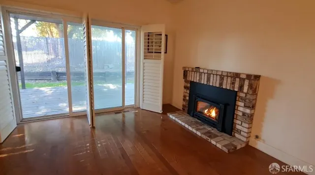 a view of an empty room with wooden floor fire place and a window