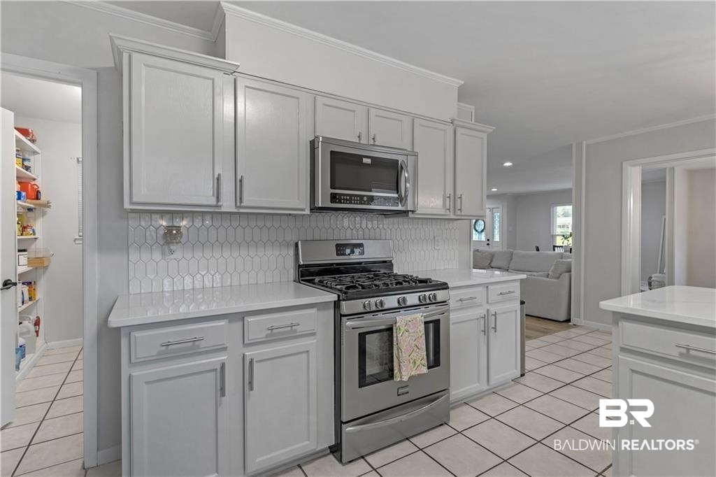 1624 Apex Drive Mobile, AL 36693 - Photo 14 of 29 Kitchen featuring crown molding, stainless steel appliances, light tile patterned flooring, and white cabinets