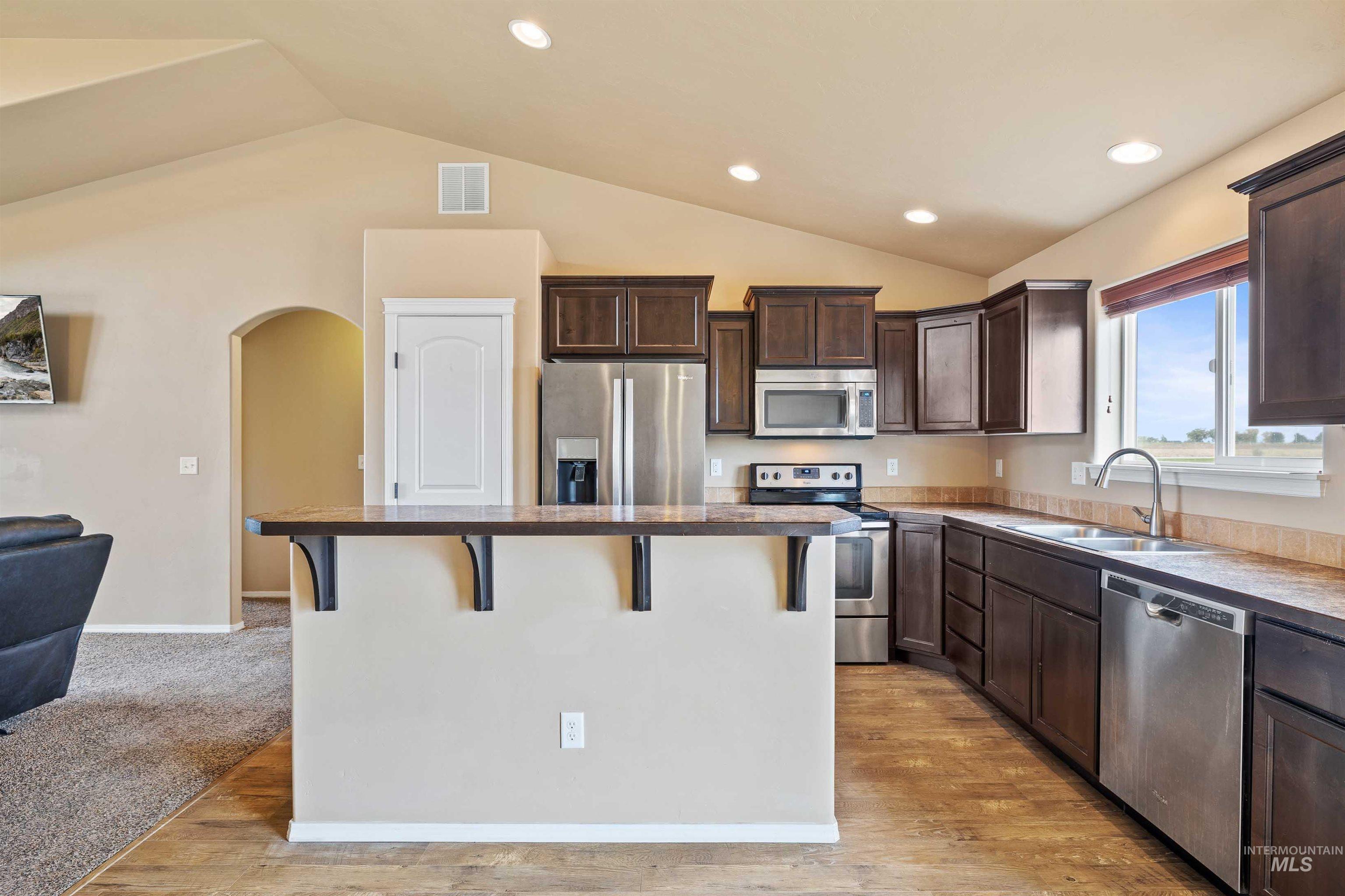 134 North 50 West Rupert, ID 83350 - Photo 8 of 36 Kitchen with dark brown cabinetry, a kitchen bar, appliances with stainless steel finishes, lofted ceiling, and light wood-type flooring