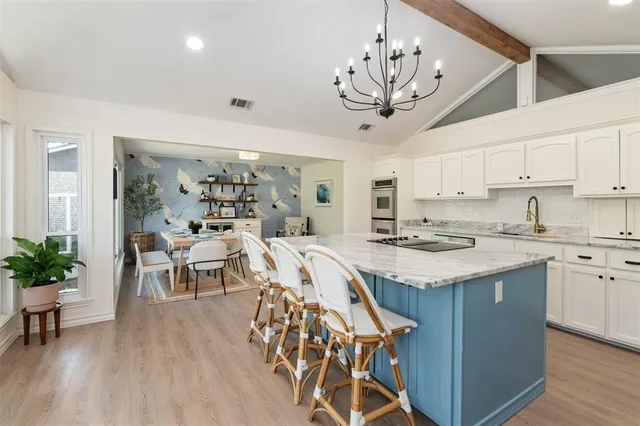 a kitchen with stainless steel appliances granite countertop a dining table chairs a chandelier and entryway