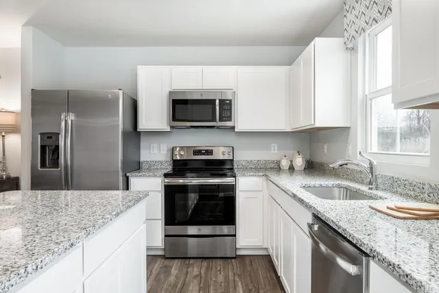 a kitchen with granite countertop a sink stainless steel appliances and white cabinets