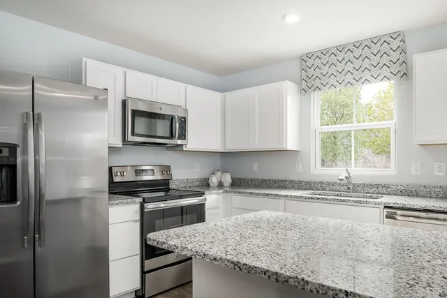 a kitchen with granite countertop a sink a counter top space cabinets stainless steel appliances and a window