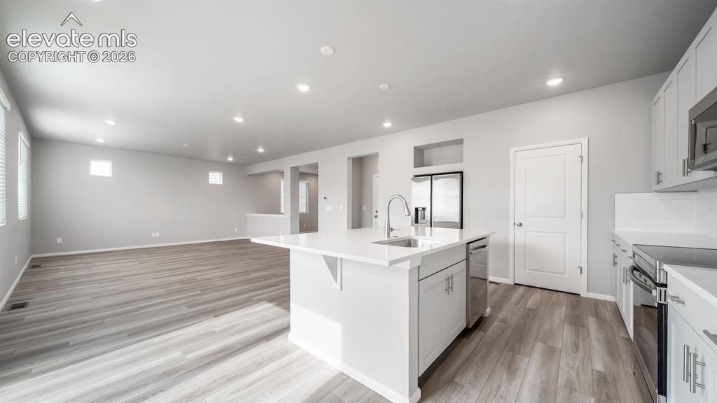 4896 Truscott Road Colorado Springs, CO 80925 - Photo 15 of 34 Spacious kitchen featuring a central island with a sink and breakfast bar, white cabinetry, integrated stainless steel appliances, and wood-finish flooringPhotos of a Model Home