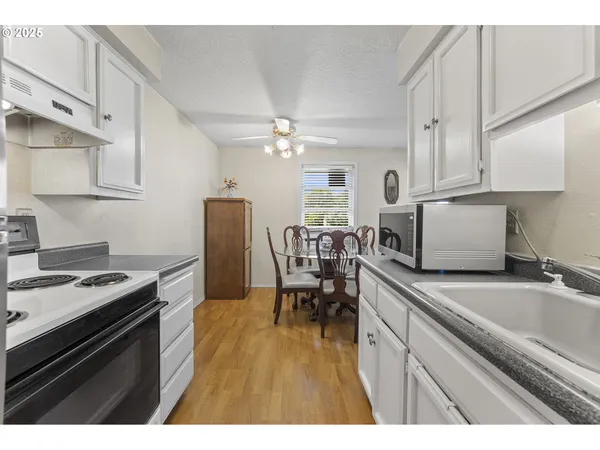 a kitchen with stainless steel appliances granite countertop a stove a sink dishwasher and white cabinets with wooden floor