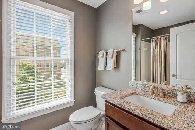 a bathroom with a granite countertop sink toilet a mirror and a large window