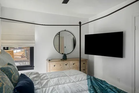 a bedroom with a bed a mirror and a flat tv screen on the dresser