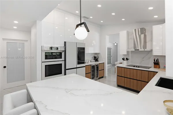 a kitchen with stainless steel appliances kitchen island granite countertop a refrigerator a sink a stove and white cabinets with wooden floor