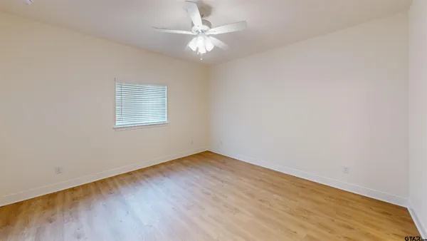 an empty room with a chandelier fan and wooden floor