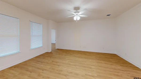 a view of an empty room with chandelier fan and wooden floor