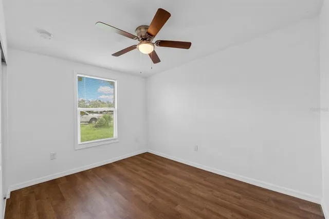 an empty room with wooden floor fan and windows