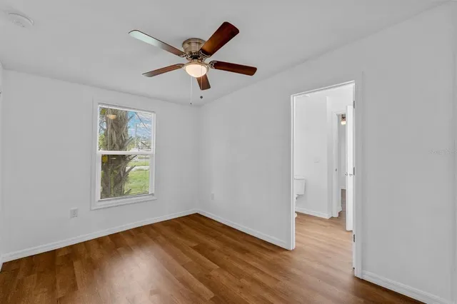 an empty room with wooden floor a ceiling fan and windows