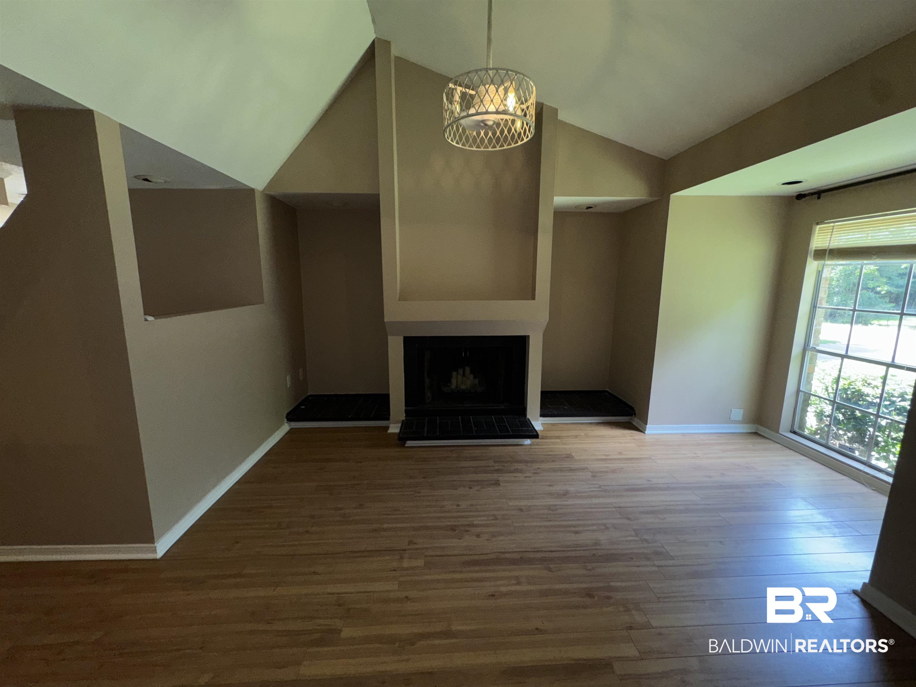 8070 Middle Ring Road Mobile, AL 36619 - Photo 18 of 26 Unfurnished living room with vaulted ceiling, wood finished floors, a chandelier, and a fireplace with raised hearth