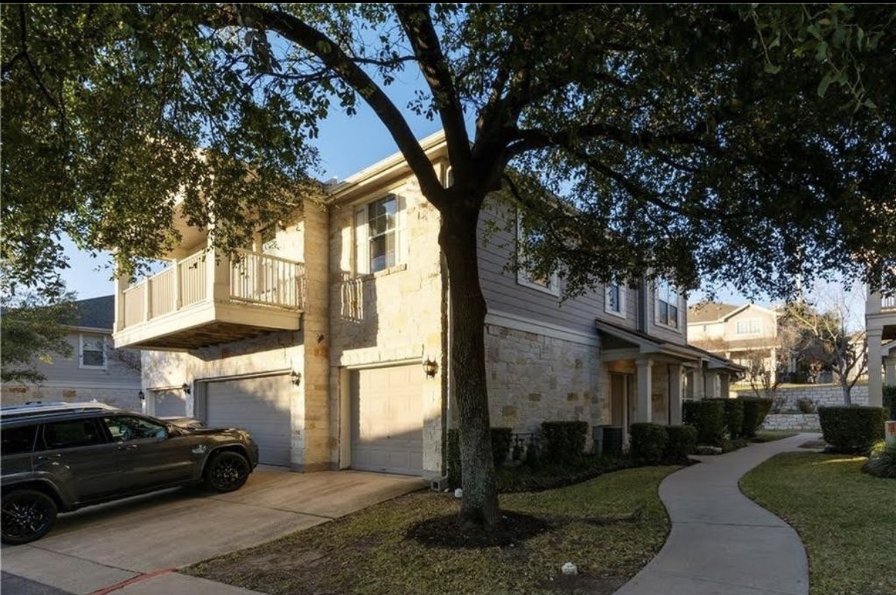 1900 Scofield Ridge Parkway, Unit 3101 Austin, TX 78727 - Photo 3 of 24 Stone and siding exterior featuring a second-story balcony with white railing, covered entry, and individual garage doors