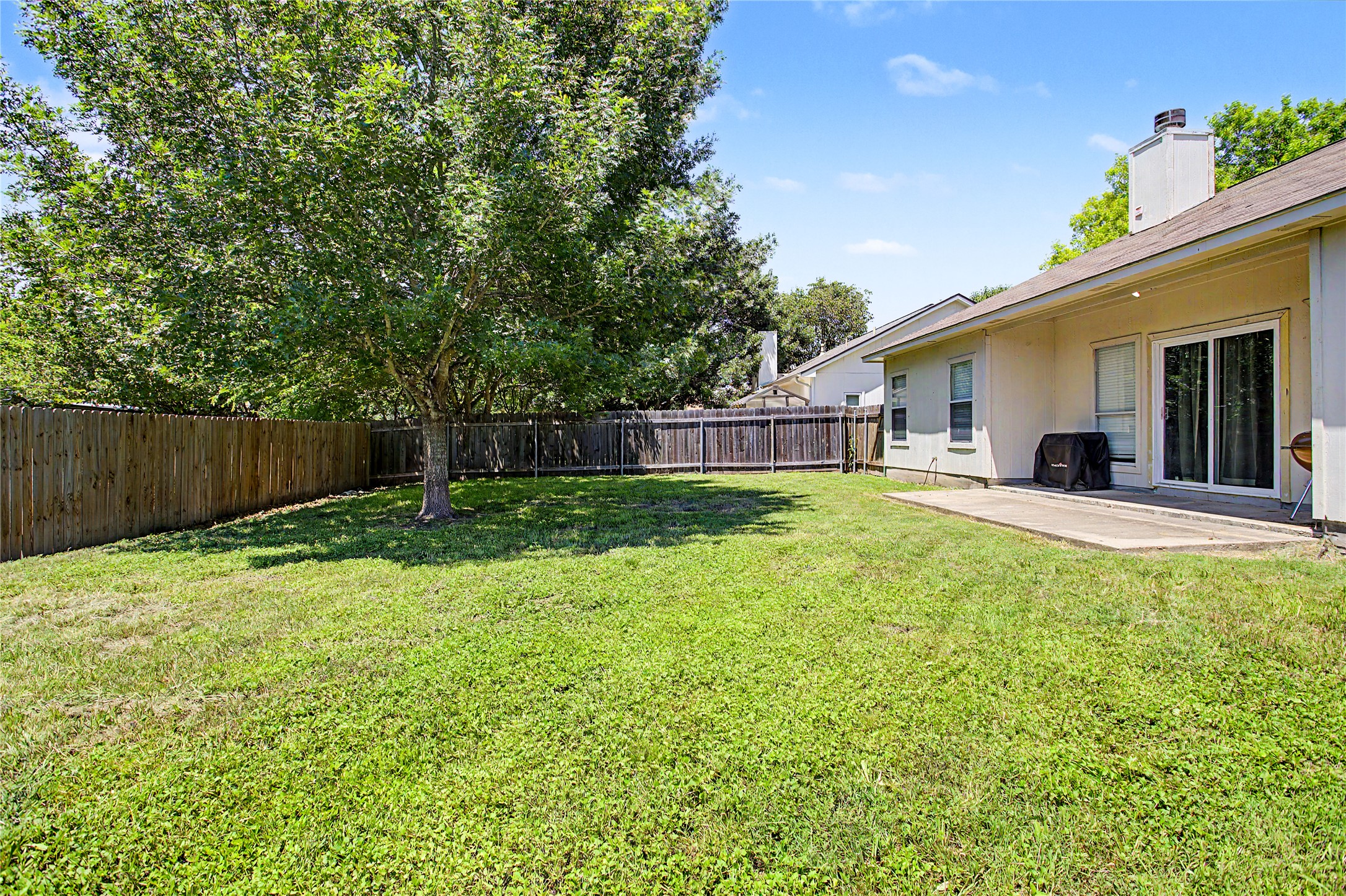 207 Kates Way Hutto, TX 78634 - Photo 22 of 24 Spacious backyard featuring a large tree providing ample shade, a full privacy fence, and a concrete patio