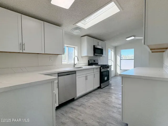 a kitchen with granite countertop a sink a counter top space stainless steel appliances and cabinets