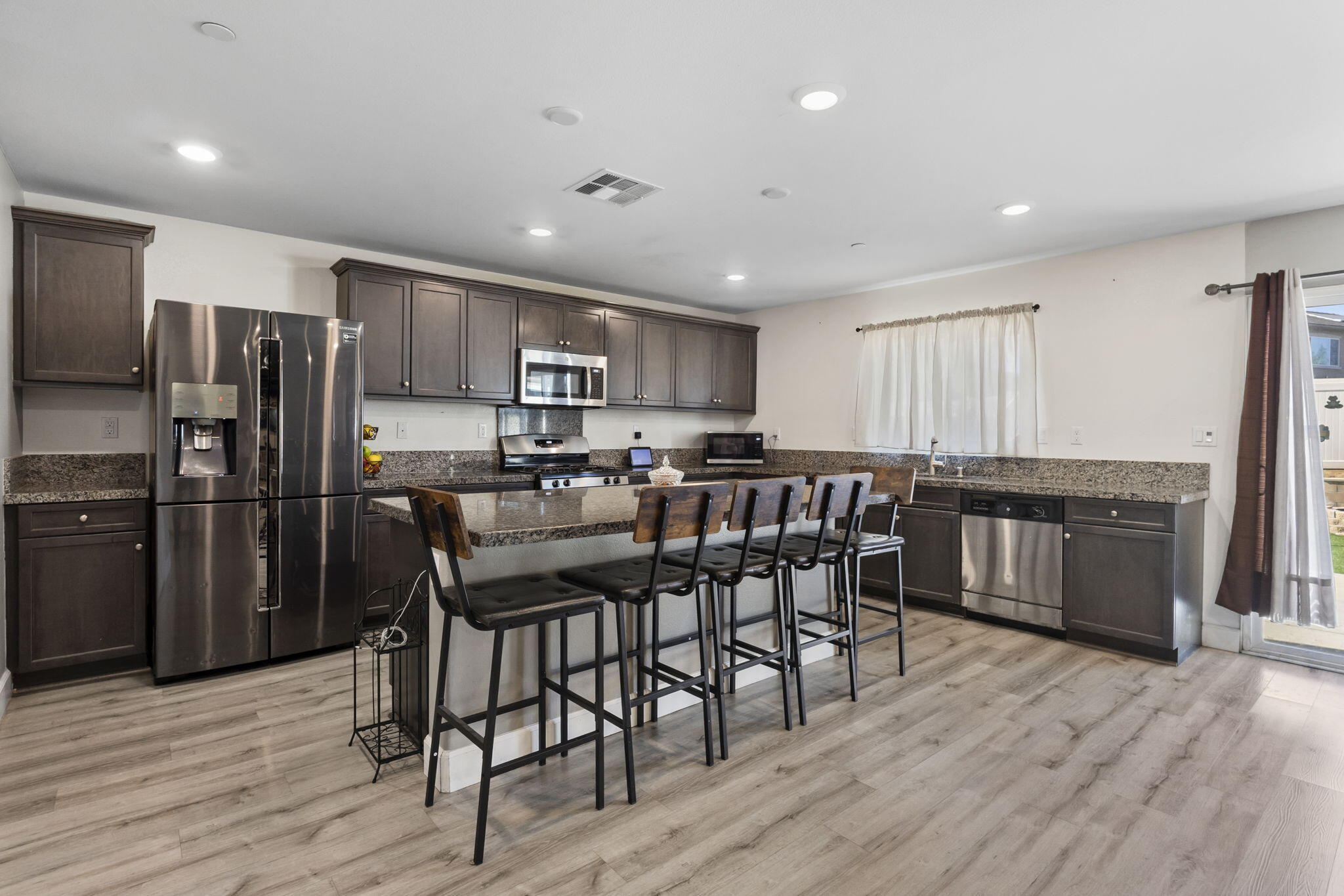 32486 Roman Warren Way Winchester, CA 92596 - Photo 21 of 45 a kitchen with stainless steel appliances kitchen island granite countertop a refrigerator a stove a sink a dining table and chairs with wooden floor