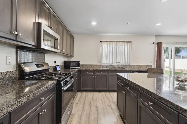 a kitchen with stainless steel appliances granite countertop a stove a sink dishwasher and cabinets with wooden floor