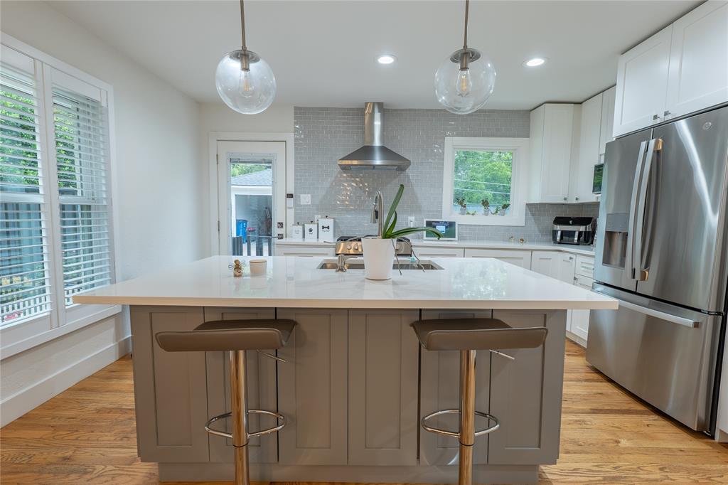 864 Peavy Road Dallas, TX 75218 - Photo 7 of 21 Kitchen featuring a large island with a light-toned countertop, stainless steel appliances, white cabinetry, a tiled backsplash, and wood-finish flooring