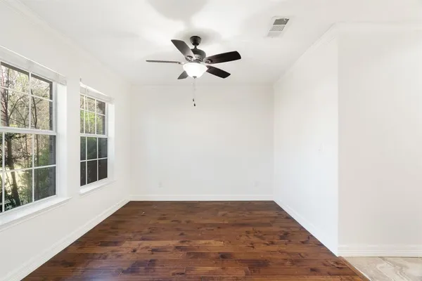 an empty room with wooden floor fan and windows