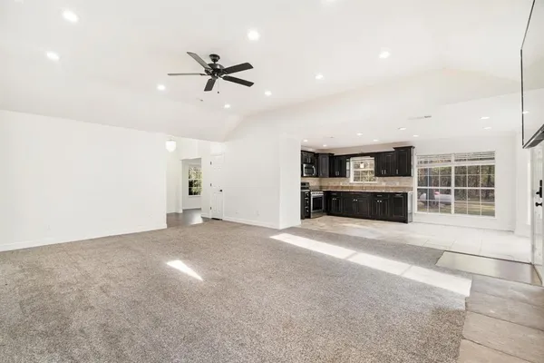 a view of a livingroom with a ceiling fan a kitchen space with a sink and windows