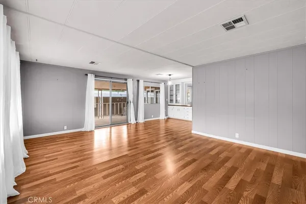 a view of empty room with wooden floor and kitchen view