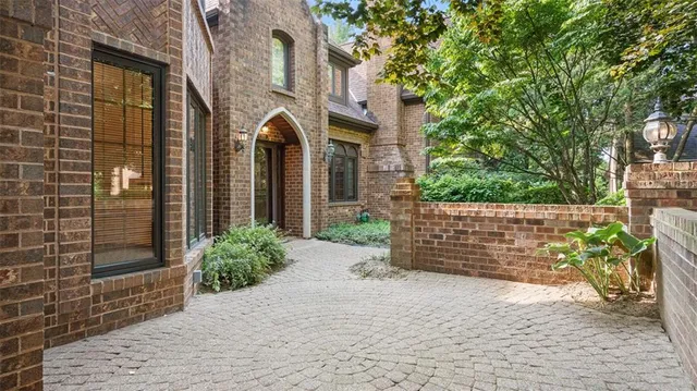 a view of a brick house with plants and large tree