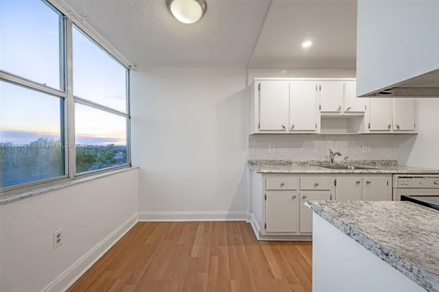 a kitchen with granite countertop white cabinets appliances a sink and a large window
