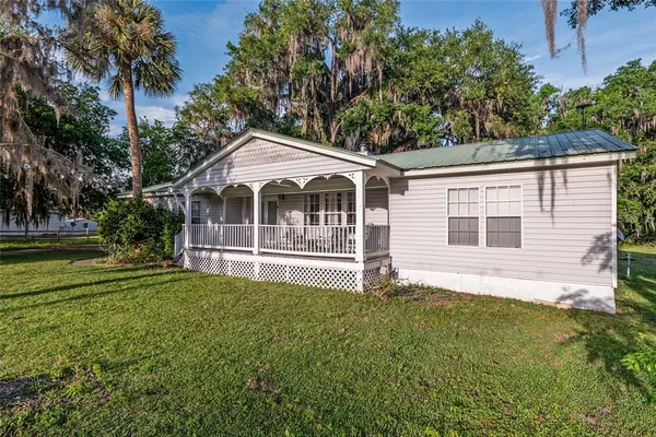 a view of a house with a small yard and wooden fence and large trees