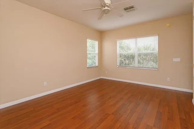 an empty room with wooden floor windows and fan