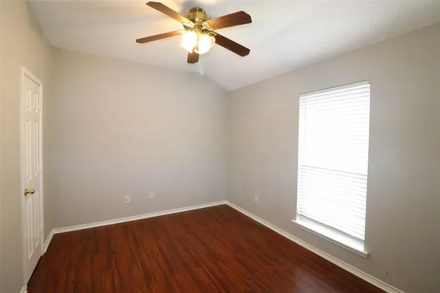 an empty room with wooden floor fan and windows