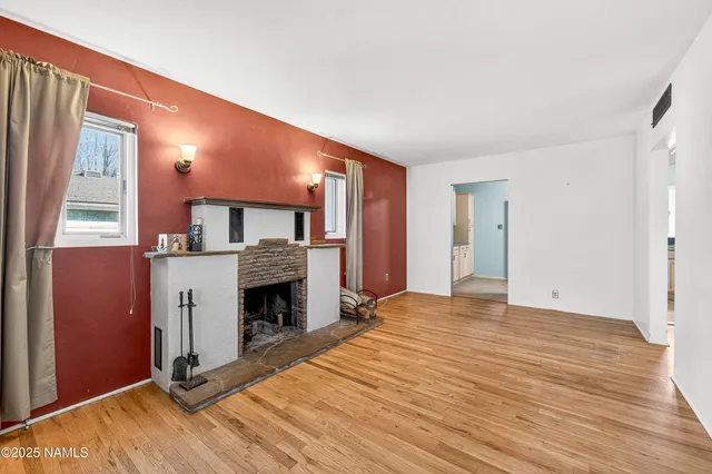 a view of an empty room with wooden floor fireplace and a window
