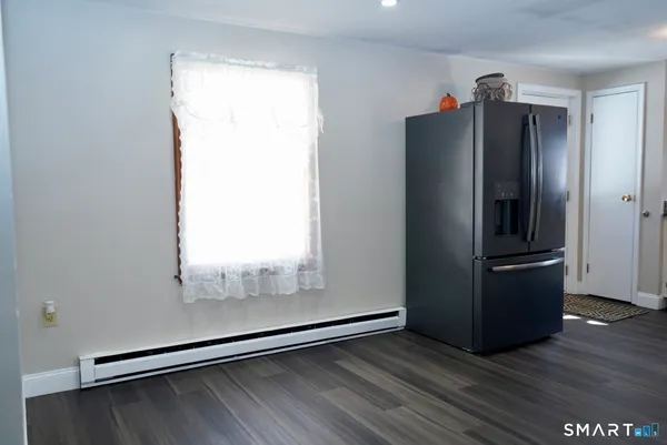 a view of a refrigerator in kitchen and an empty room with wooden floor