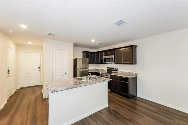 a kitchen with stainless steel appliances granite countertop a stove top oven a sink dishwasher and a refrigerator with wooden floor