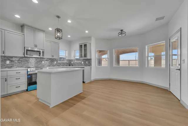 a kitchen with stainless steel appliances granite countertop a stove a sink dishwasher a refrigerator and white cabinets with wooden floor