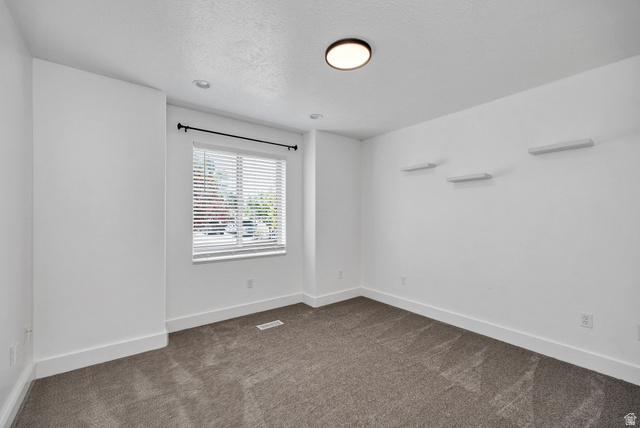 2912 South 1080th Street West Logan, UT 84321 - Photo 7 of 43 Neutral-toned carpeted room featuring a single window with blinds, a black curtain rod, and three wall-mounted shelves