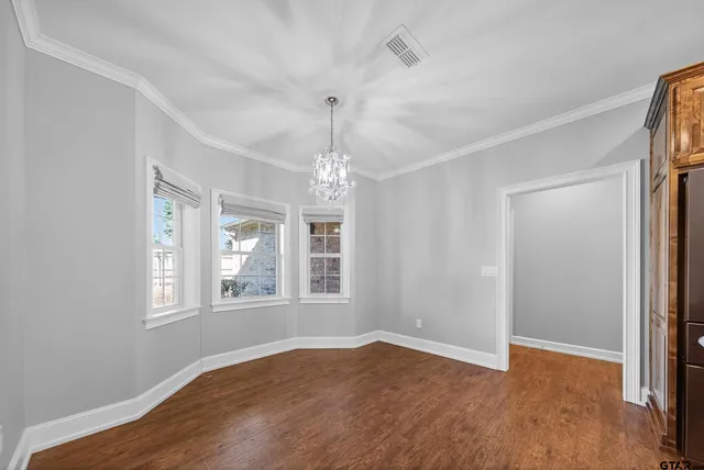 an empty room with wooden floor chandelier and windows