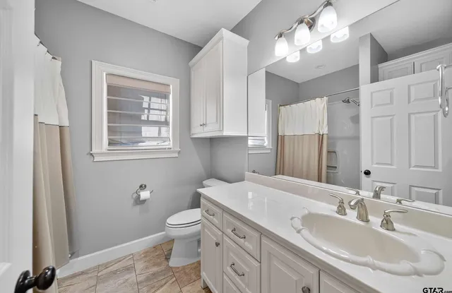 a bathroom with a granite countertop toilet a sink a light fixture and a window