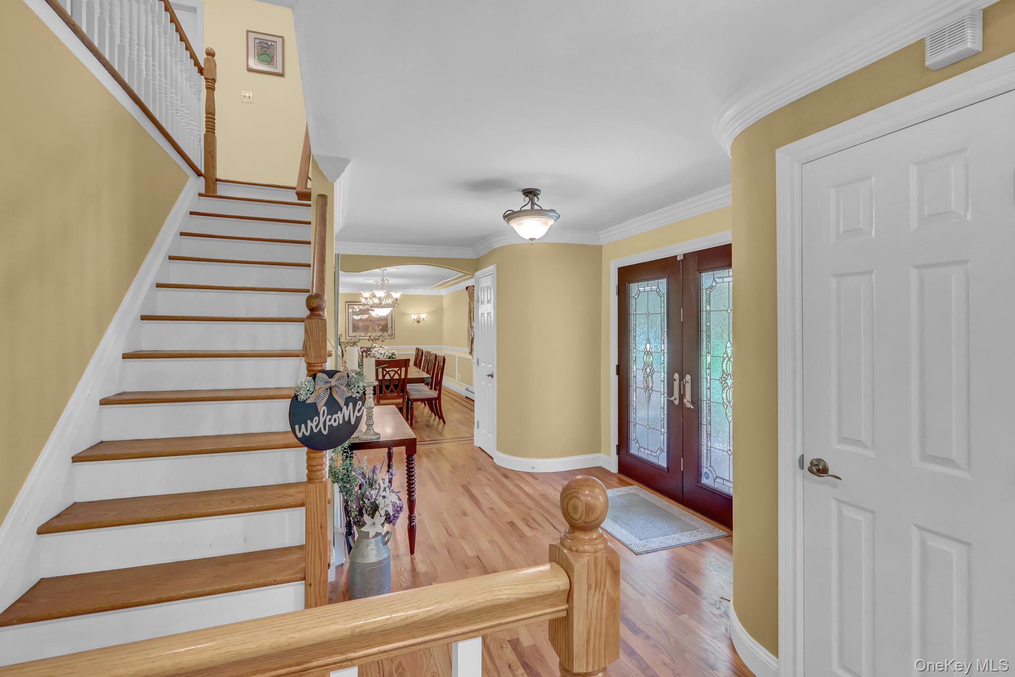 15 Stillwater Road Nissequogue, NY 11780 - Photo 5 of 43 Entry foyer featuring hardwood flooring, a grand staircase with wood treads and white risers, decorative glass double entry doors, a curved wall, and crown molding