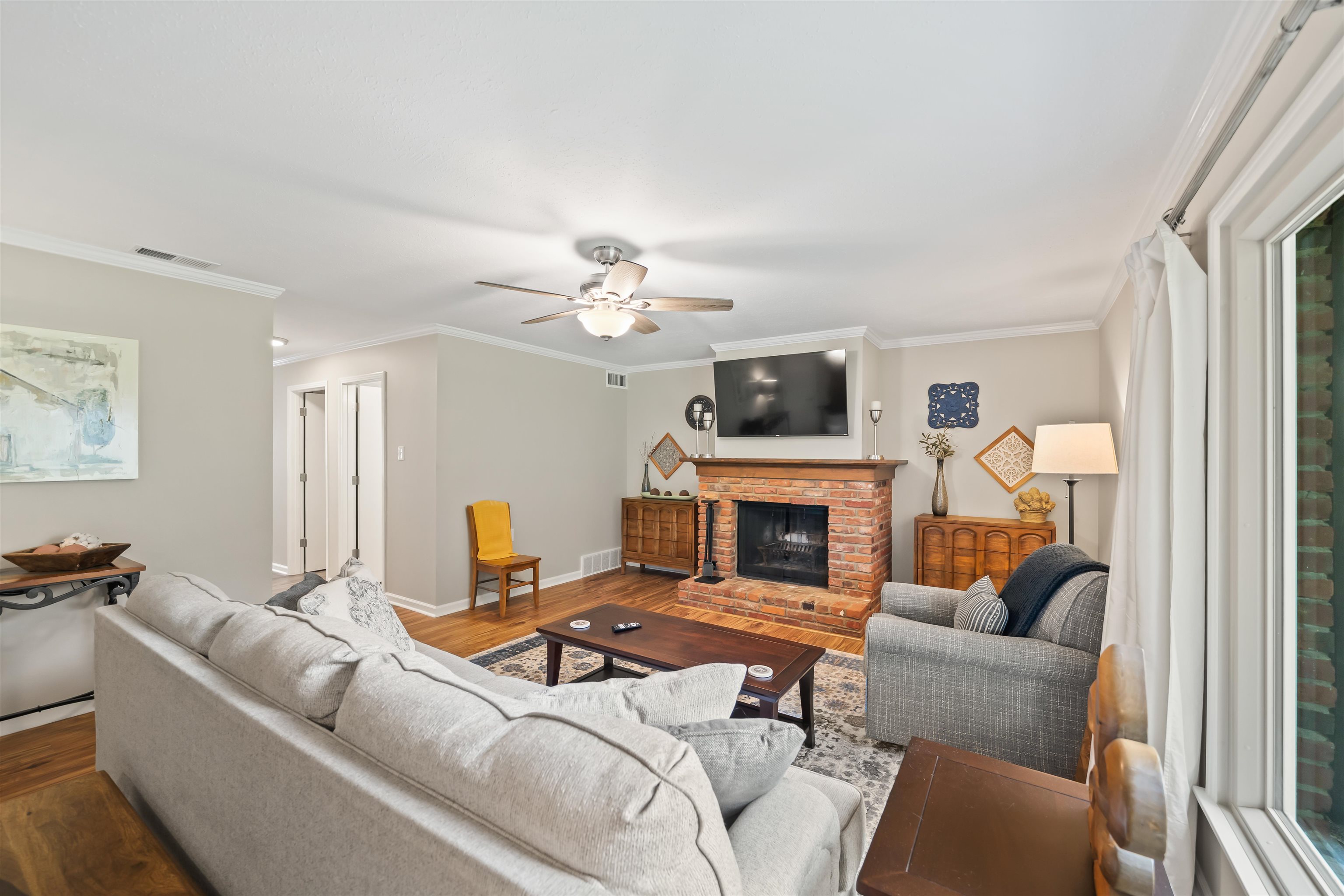 6943 Fords Station Road, Unit 64 Germantown, TN 38138 - Photo 7 of 30 Brick fireplace with a wood mantel, wood-finish flooring, white crown molding, light-colored walls, and a ceiling fan with integrated lighting
