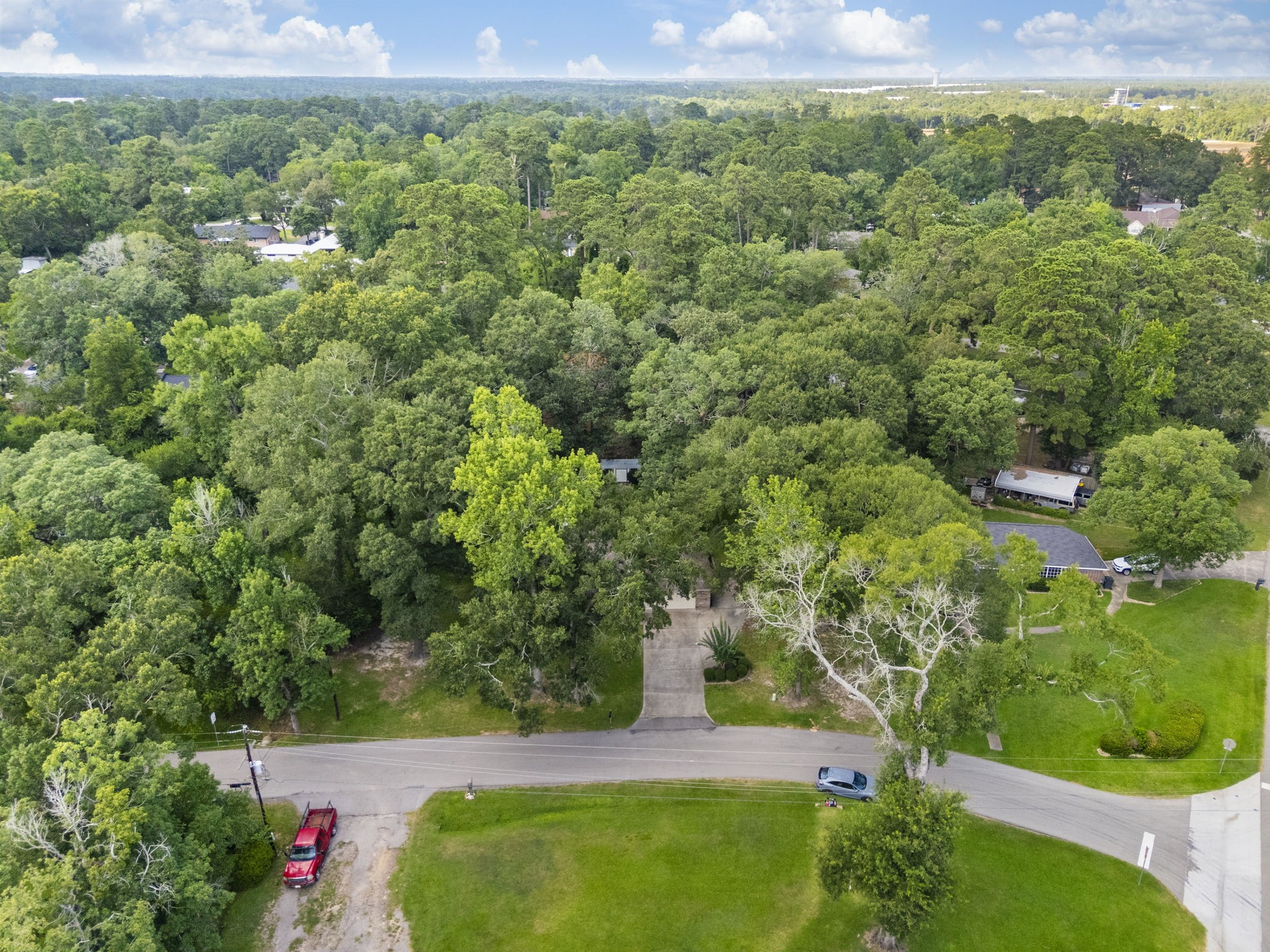 202 Sunset Boulevard Conroe, TX 77303 - Photo 48 of 50 This aerial photo showcases a lush, wooded neighborhood with mature trees providing a serene, natural setting. A curving road runs through the area, and there are a few homes visible among the greenery, offering a sense of privacy and tranquility.