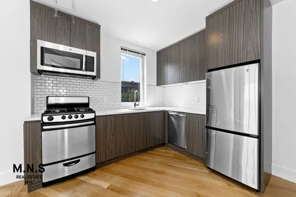 a view of an empty room with kitchen and a window