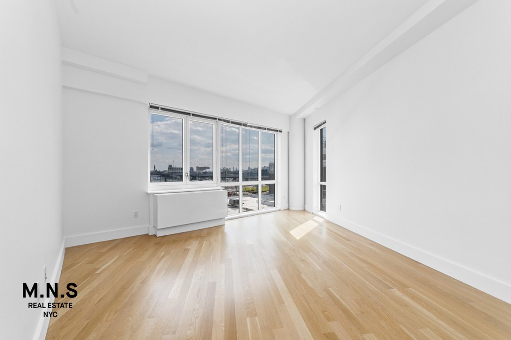 37-14 36th Street, Unit 7Q Queens, NY 11101 - Photo 5 of 20 an empty room with wooden floor and windows