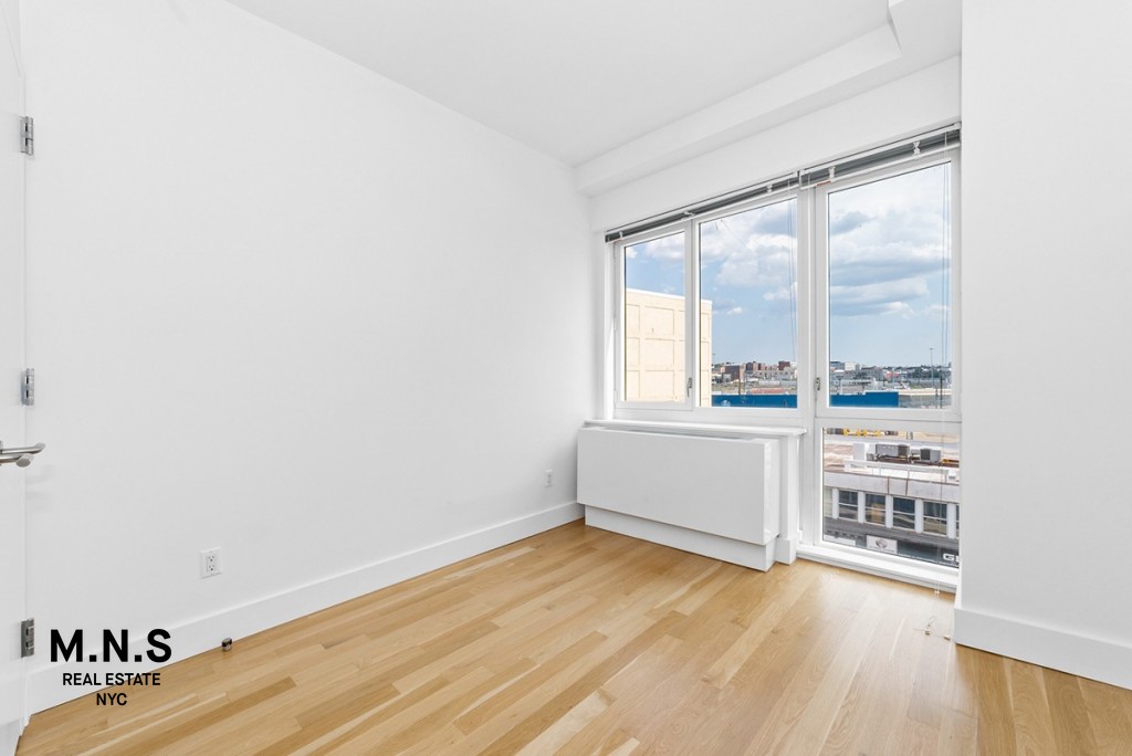 37-14 36th Street, Unit 7Q Queens, NY 11101 - Photo 6 of 20 an empty room with wooden floor and windows