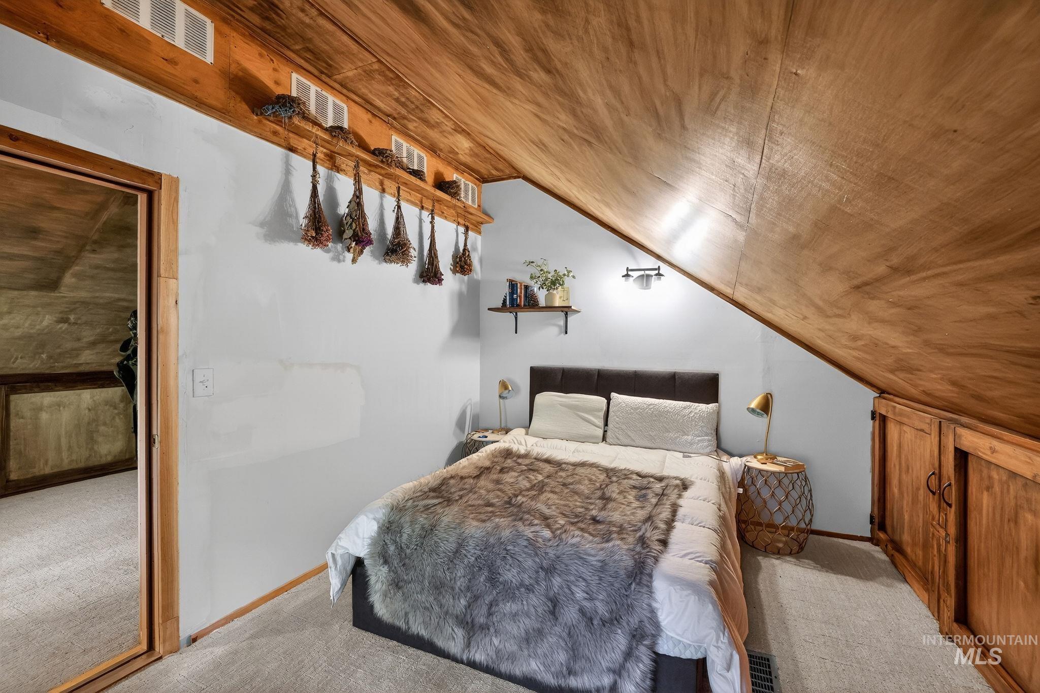 321 Secesh River Road McCall, ID 83638 - Photo 18 of 50 Carpeted room featuring a sloped wood-finish ceiling, built-in wooden cabinetry, a wall-mounted light fixture, and a floating shelf